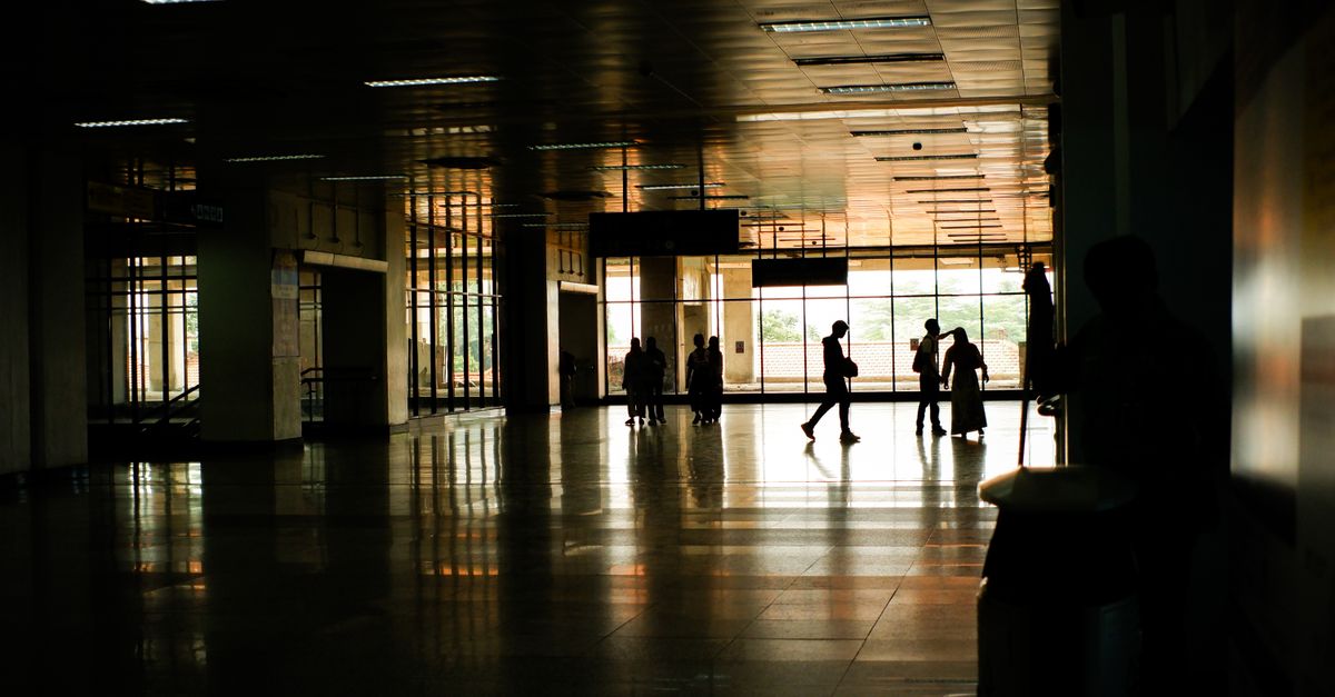 The main subject of the photograph appears to be a group of people walking through a large, well-lit room with windows along one side.