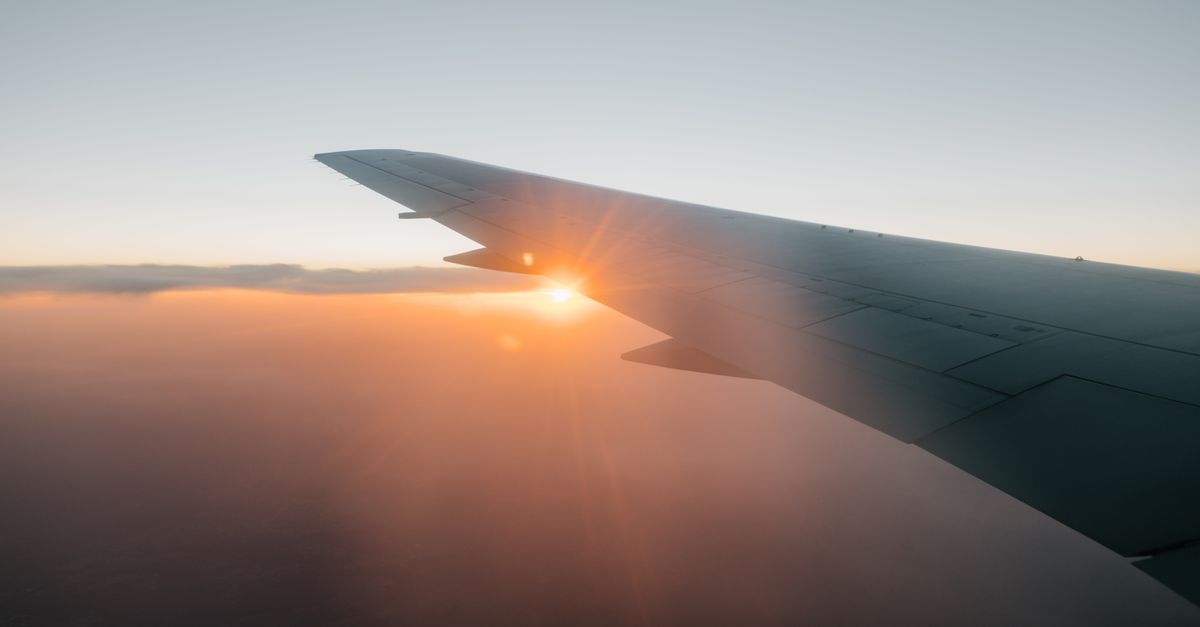 Through airplane window of wing on background of sundown sky with orange sun