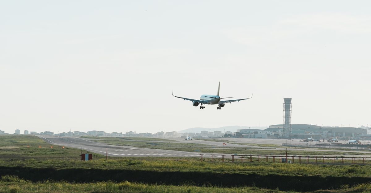 A passenger airplane lands on a runway with a control tower in the background, clear daytime view.