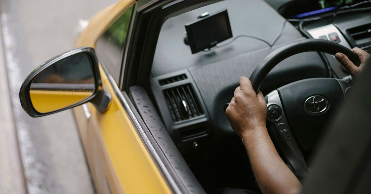 From above of crop unrecognizable person driving modern yellow taxi car with GPS navigator on city street in daytime