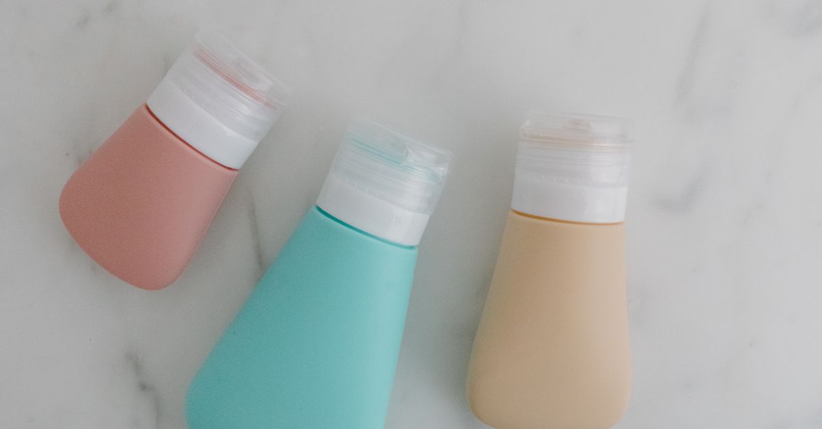 Three small travel-size toiletry bottles laid out on a marble surface