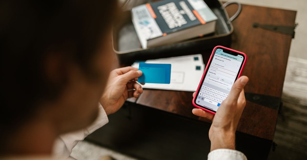Person entering payment details on a phone next to a bank card, managing an online booking