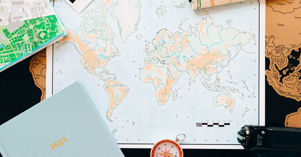 Flat lay of travel essentials including a world map, compass, and planner, perfect for planning your next adventure.