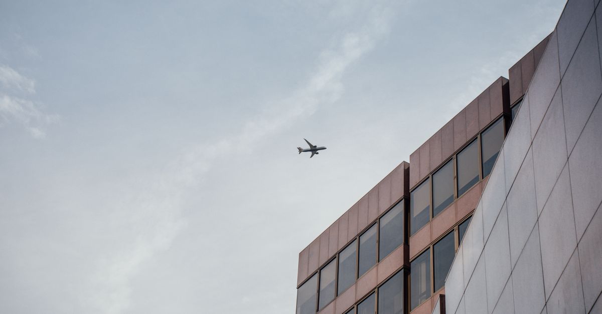 Airplane flying over modern office building with clear sky backdrop in London, England.