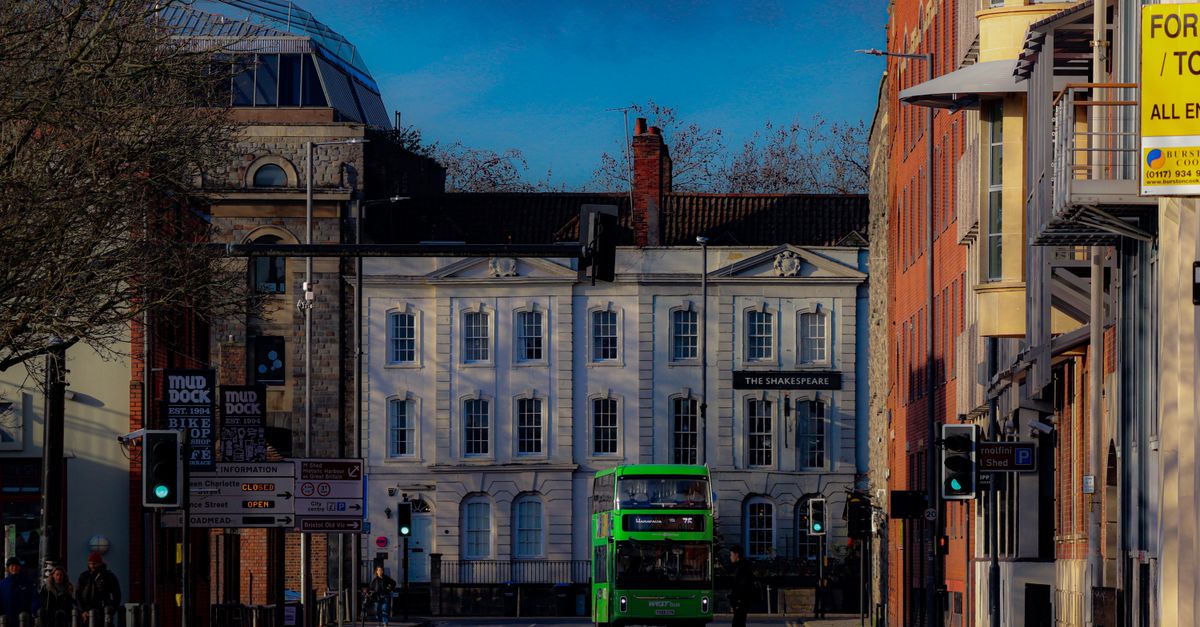 A vibrant city street featuring a green bus in front of architectural buildings in Bristol.