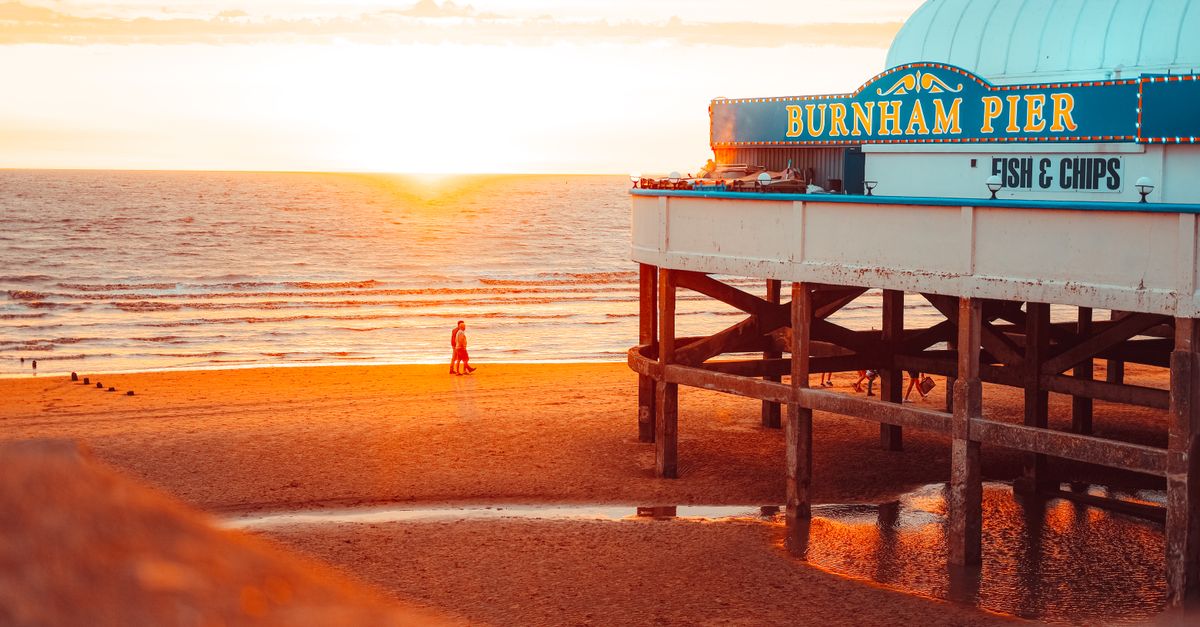 Warm sunset view of Burnham Pier with beachgoers and scenic coastal horizon.