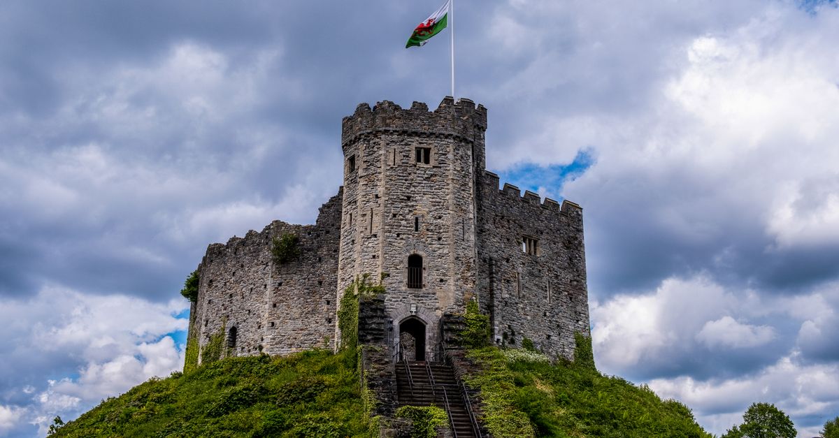Cardiff Castle's Norman keep on its motte, Welsh flag flying, against a cloudy sky