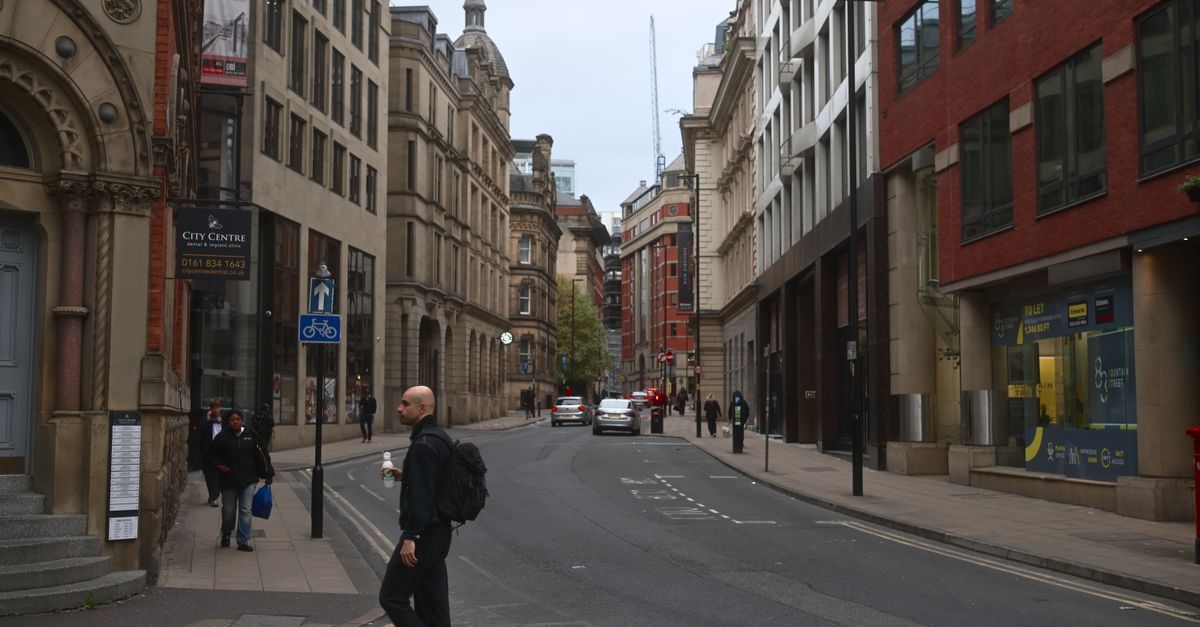 A man crossing the street in Manchester's city centre, with historic architecture.