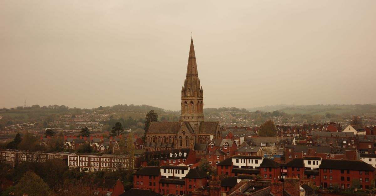 Aerial view of a historic Gothic church amidst a gloomy English urban landscape.