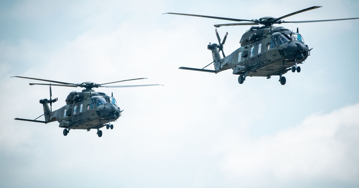 Two military helicopters flying in formation against a blue sky.