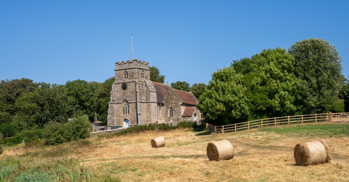 Charming stone church in Kington Magna, England, surrounded by hay bales and lush trees.