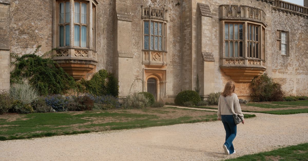 A woman walks by the historic Lacock Abbey, showcasing its stunning architecture.