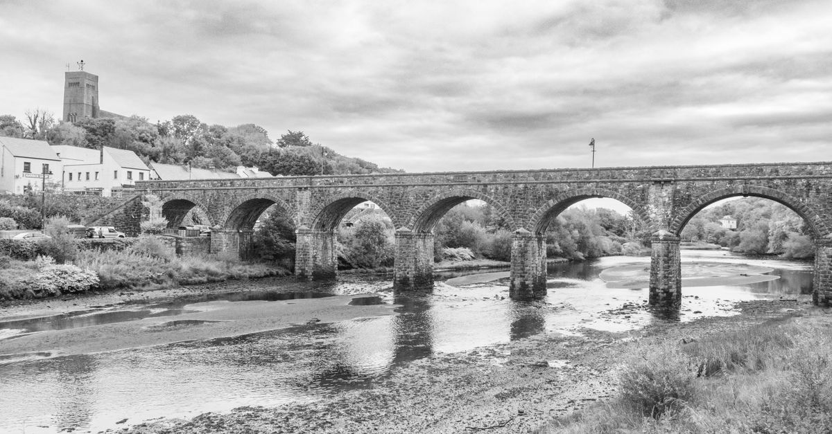 Black and white photo of a historic stone bridge over a river in Newport, County Mayo.