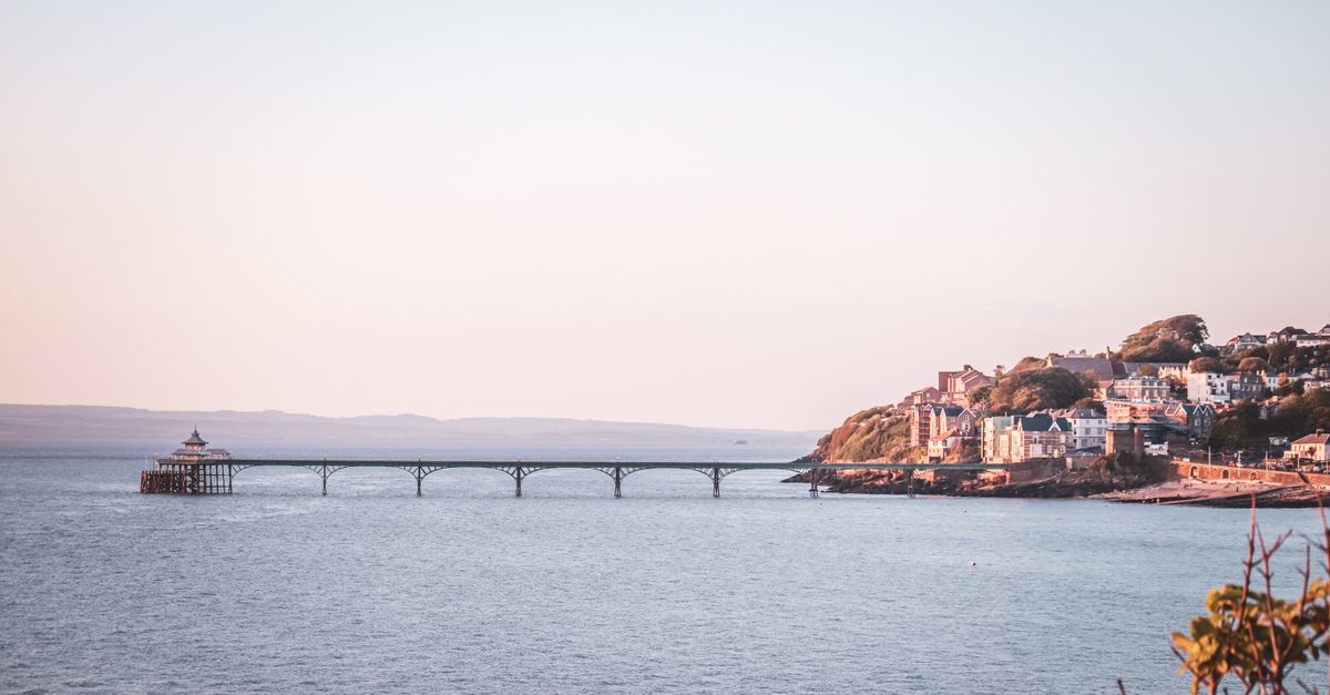 Clevedon Pier stretching out into the Bristol Channel at sunset, with the town on the headland behind it.