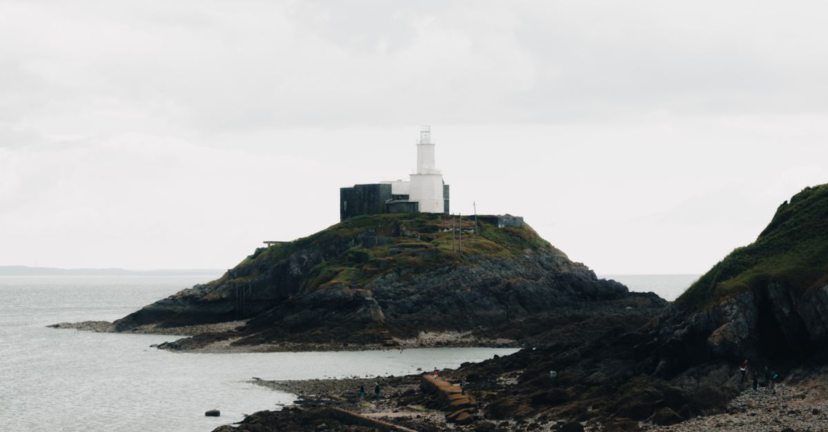 Scenic view of a lighthouse perched on a rocky coastline under a cloudy sky.
