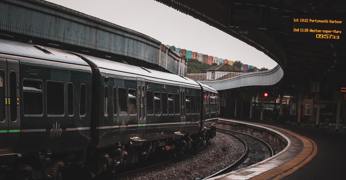 A Great Western Railway train curving into a platform at Bristol Temple Meads, with the honest departure board overhead.