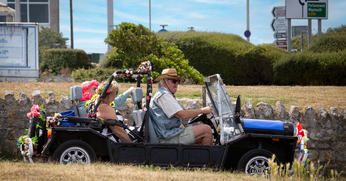 A decorated vintage car with passengers enjoys a sunny day drive in the English countryside.