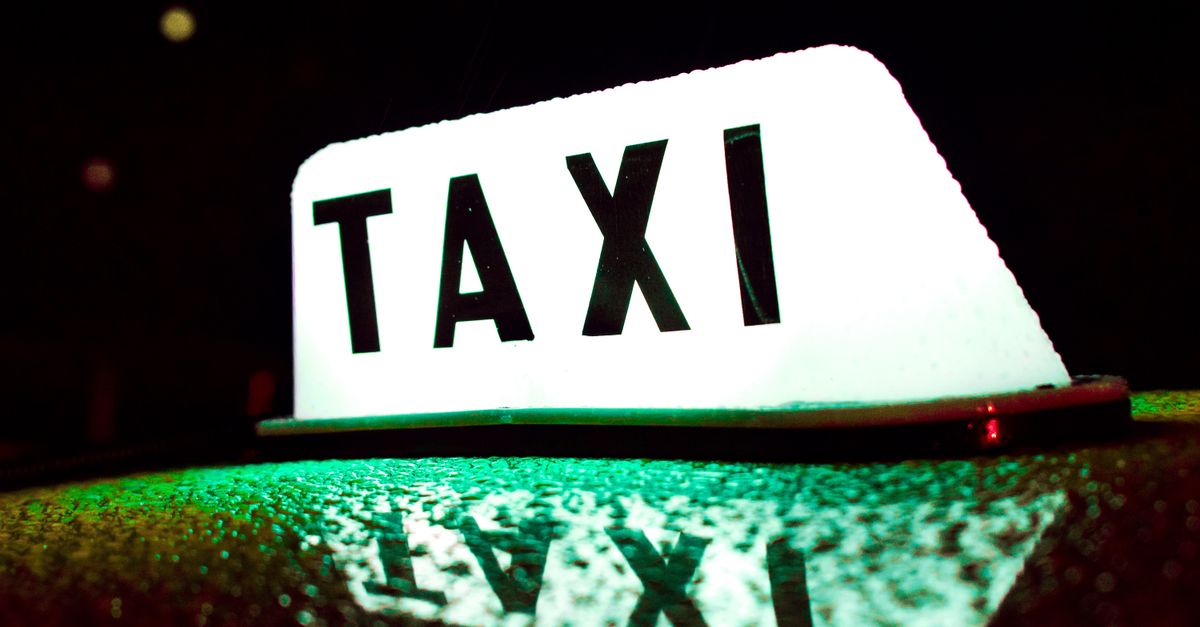 Illuminated 'TAXI' roof-light sign glowing green on a car roof at night