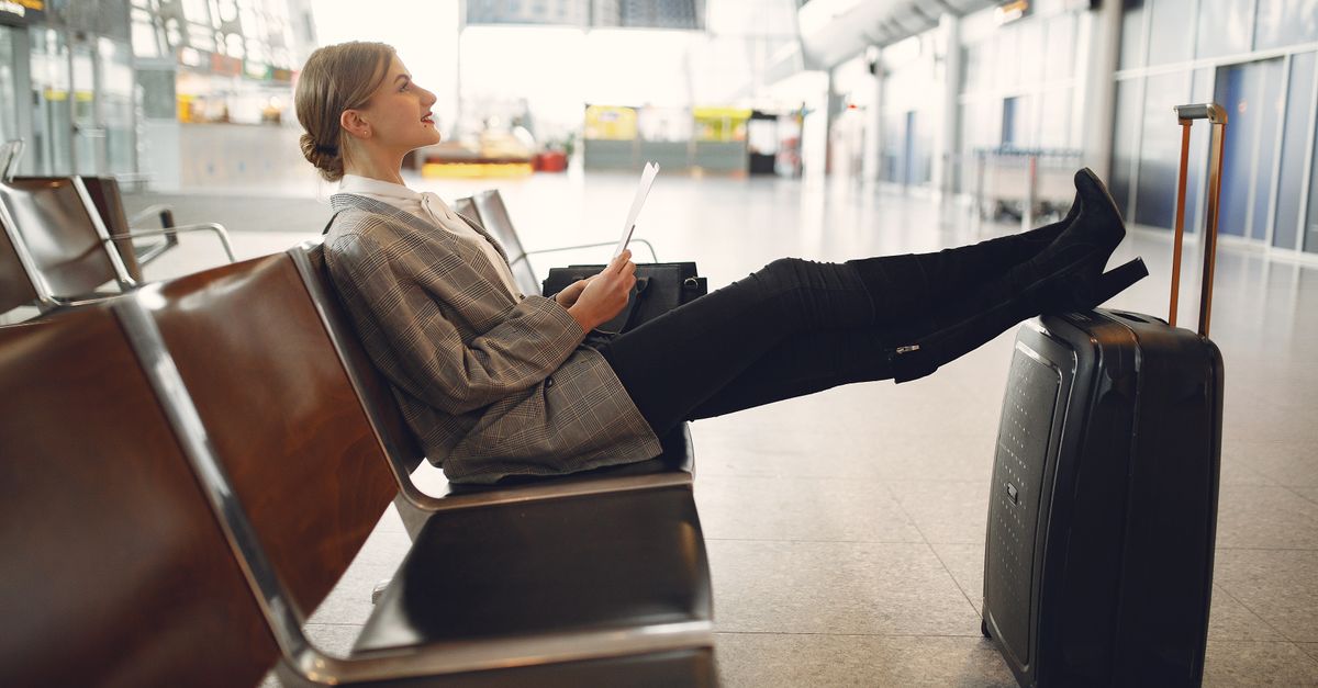 Relaxed traveller with her feet up on a suitcase in an airport terminal, smiling and reading a document