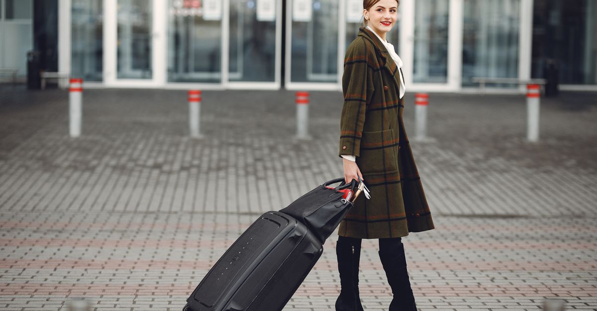 Traveller wheeling a suitcase outside a modern airport terminal entrance
