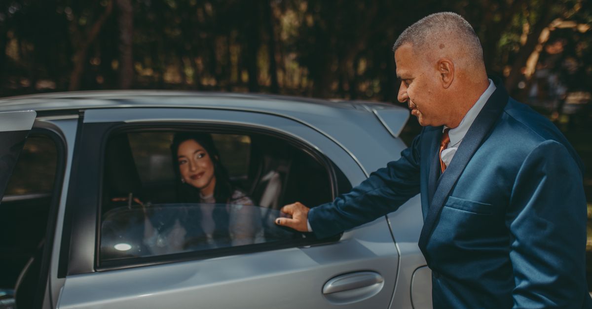 A suited driver holding the rear car door open for a passenger