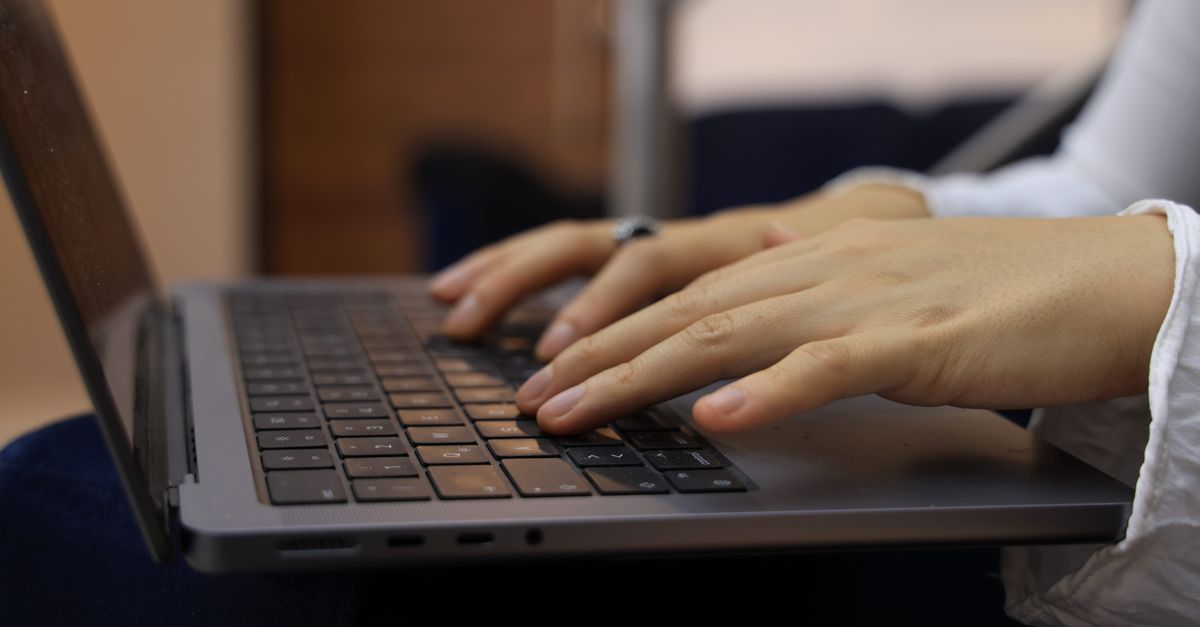 Close-up of hands typing on a laptop keyboard, representing staying connected while travelling