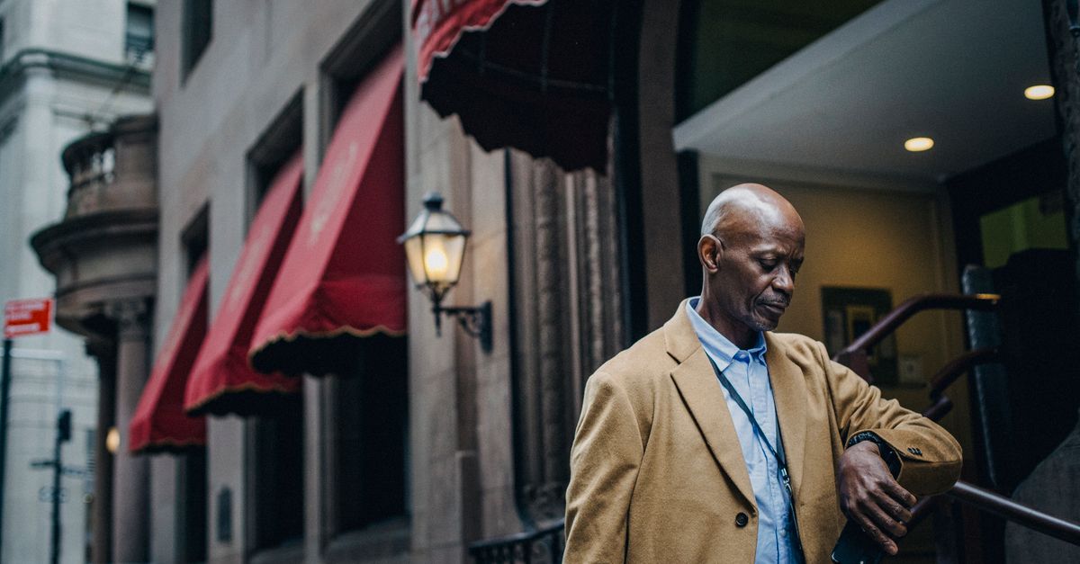 A man checking his watch while waiting on a street, visibly impatient.