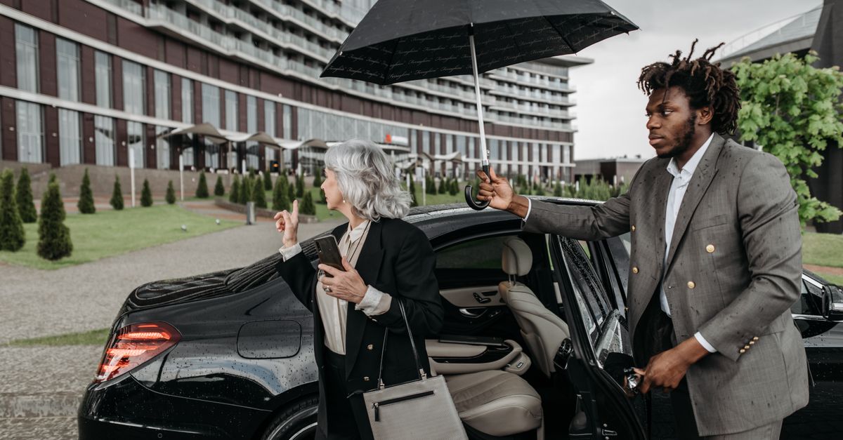 A chauffeur holding an umbrella for a business traveller getting into a premium car.